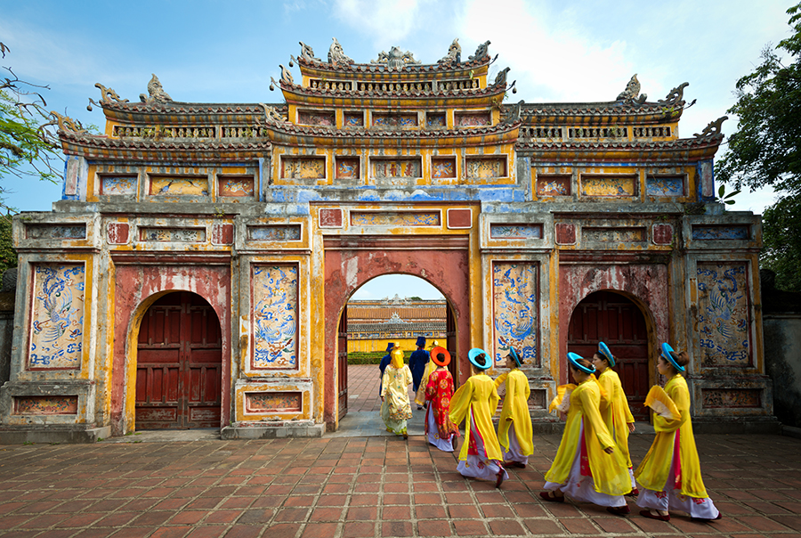 People in traditional costumes walk under an archway in the Imperial City of Hue with Man Nguyen Private Vietnam Tour Packages